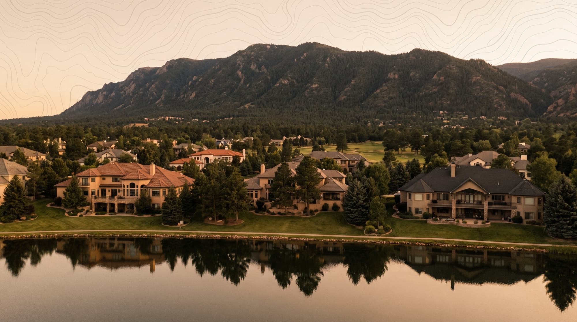 Upscale estate homes beside a lake at the forested foot of Cheyenne Mountain in the Broadmoor area of Colorado Springs at dusk