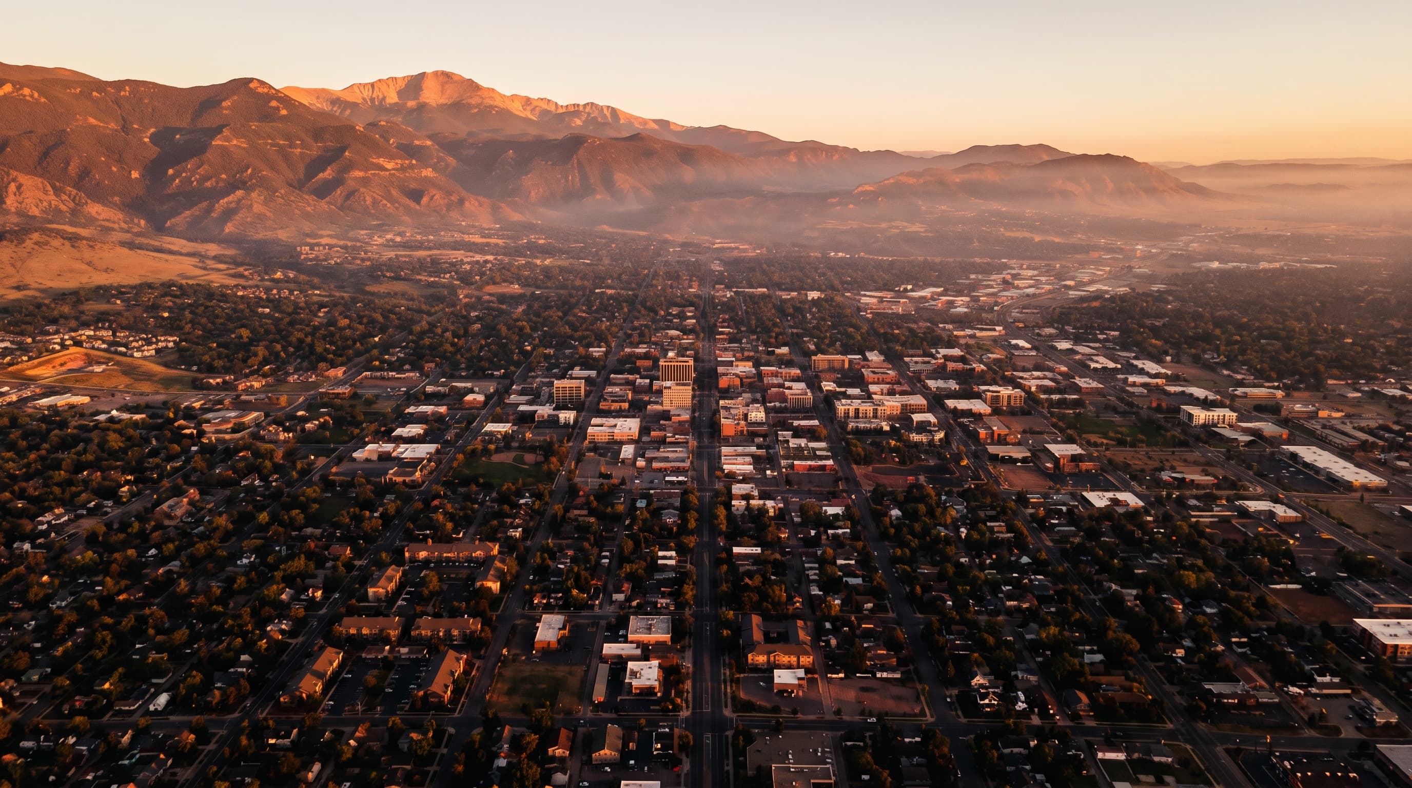 Aerial view of Colorado Springs at golden hour with the Front Range and Pikes Peak beyond